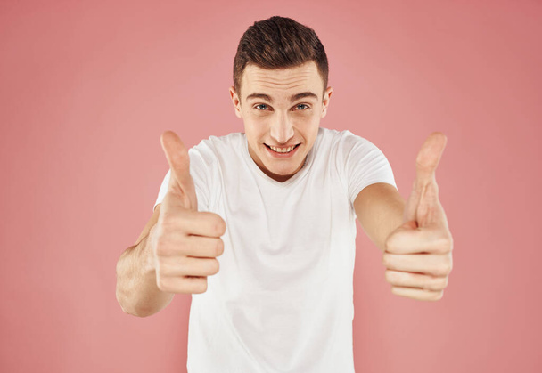 Guy on a pink background gesturing with his hands in a white t-shirt cropped view - Φωτογραφία, εικόνα