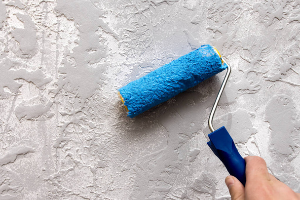 painting a gray textured wall with a roller in blue paint. close-up. renovation concept. - Photo, Image