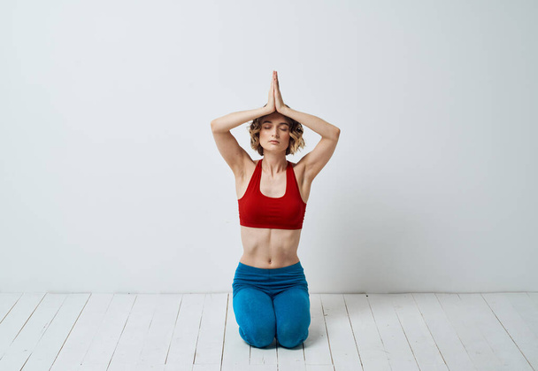 Uma mulher senta-se em um assoalho claro dentro com suas mãos juntando asanas do ioga para o relaxamento - Foto, Imagem