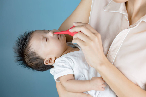 мать чистит нос новорожденному красным резиновым мячом - Фото, изображение