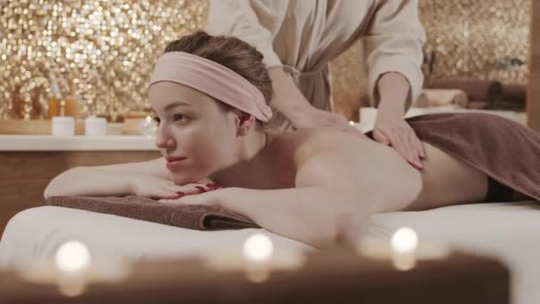 Zamknięcie młodej atrakcyjnej białej kobiety leżącej na stole do masażu w centrum spa i cieszącej się odmładzającym masażem pleców - Materiał filmowy, wideo
