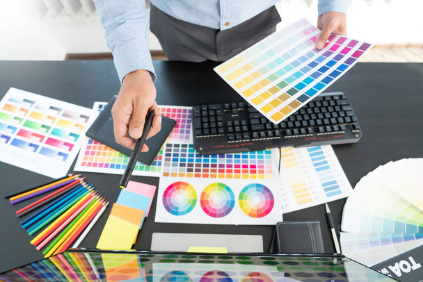 δημιουργικός γραφίστας που επιλέγει χρωματική κλίμακα για επεξεργασία έργων τέχνης ενώ εργάζεται στο γραφείο - Φωτογραφία, εικόνα