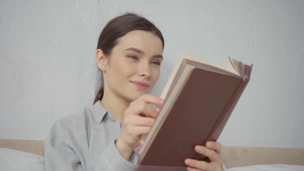 heureux jeune femme retournant pages tout en lisant le livre à la maison - Séquence, vidéo