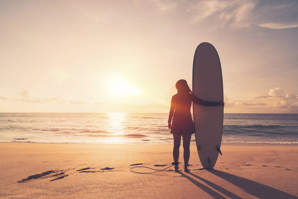 Donna tenere tavola da surf in piedi al tramonto tropicale sfondo spiaggia. Vacanze estive e sport concetto avventuroso. Vintage tono effetto filtro colore stile. - Foto, immagini