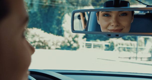 χαρούμενη γυναίκα χαμογελώντας και κοιτάζοντας στον καθρέφτη του αυτοκινήτου - Φωτογραφία, εικόνα