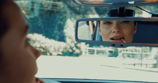 blurred and happy woman applying lip gloss while looking in rearview mirror  - Zdjęcie, obraz
