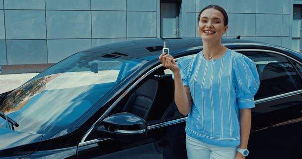 ευτυχισμένη νεαρή γυναίκα κρατώντας το κλειδί αυτοκινήτου κοντά στο νέο αυτοκίνητο - Φωτογραφία, εικόνα