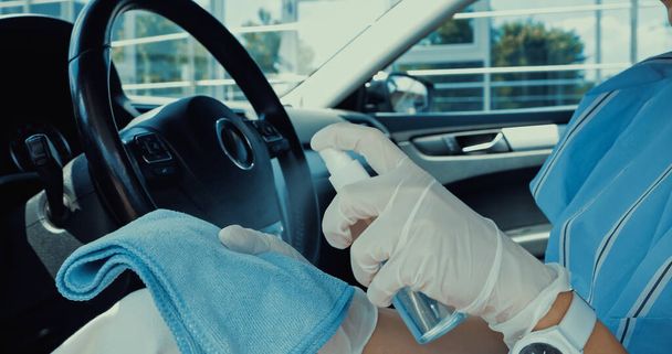 bijgesneden weergave van de vrouw in latex handschoenen spuiten ontsmettingsmiddel op doek - Foto, afbeelding