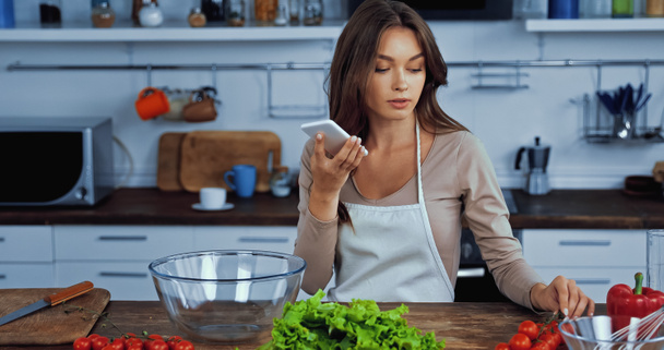 woman using voice assistant while holding smartphone near ingredients  - Zdjęcie, obraz