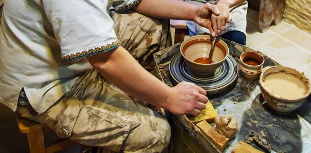 the Hands of a master and a student make a pitcher on a Potters wheel of yellow clay. Selective focus on hands - Photo, Image