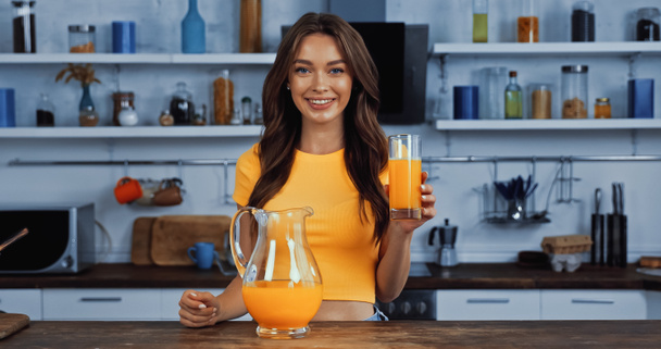 веселая молодая женщина держит кувшин с апельсиновым соком и стаканом - Фото, изображение