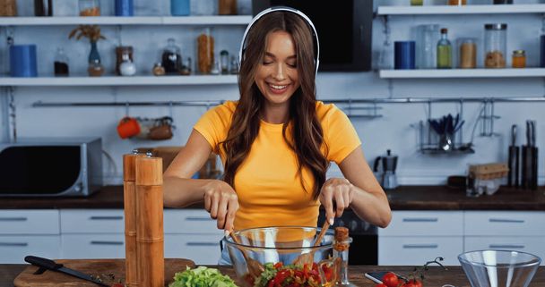happy woman in wireless headphones listening music and mixing salad - Photo, Image