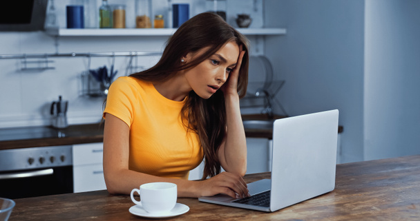 upset freelancer using laptop near cup of coffee - Photo, Image