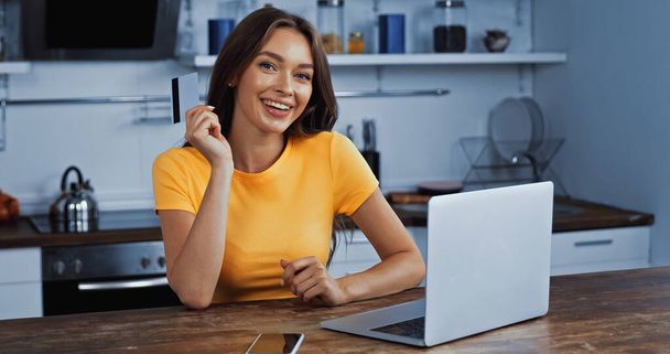 mujer feliz usando el ordenador portátil y la celebración de la tarjeta de crédito mientras que las compras en línea  - Foto, Imagen