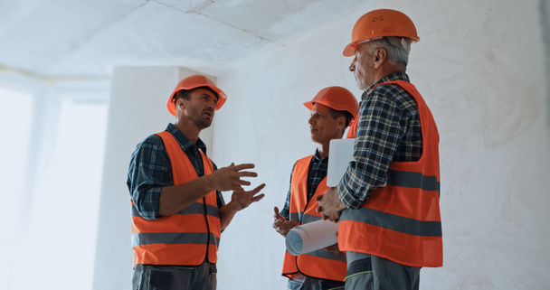 Οικοδόμος gesturing ενώ μιλάμε με συναδέλφους σε σκληρά καπέλα στο εργοτάξιο - Φωτογραφία, εικόνα