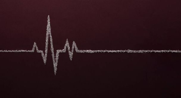 Kırmızı zemin üzerinde beyaz şeker kullanarak kalp atış hızı grafiği - Fotoğraf, Görsel