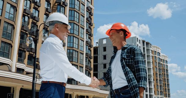 зрелый инженер и строитель пожимает руку и разговаривает на строительной площадке - Фото, изображение