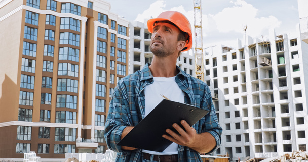 bouwer in hard hat holding klembord op bouwplaats - Foto, afbeelding