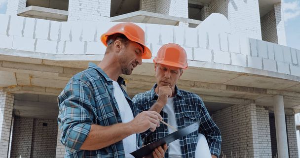 Bauarbeiter schauen auf Klemmbrett und reden auf Baustelle - Foto, Bild