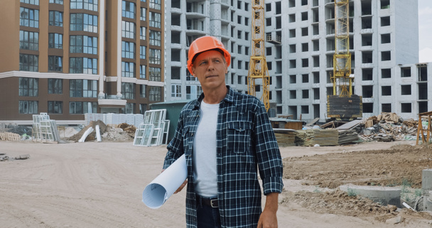 зрілий будівельник тримає відбиток і стоїть на будівельному майданчику
 - Фото, зображення