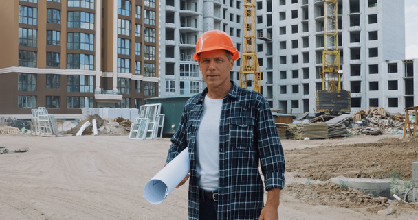 constructor de mediana edad sosteniendo plano y de pie en el sitio de construcción - Foto, Imagen