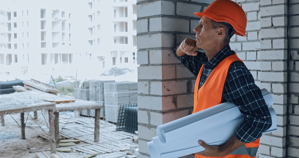 Pensive builder in helmet holding blueprints on construction site - Fotografie, Obrázek