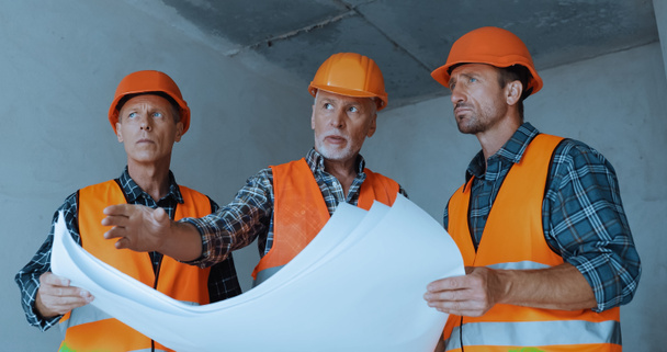 Builders in safety helmets talking near blueprints on construction site - Photo, Image