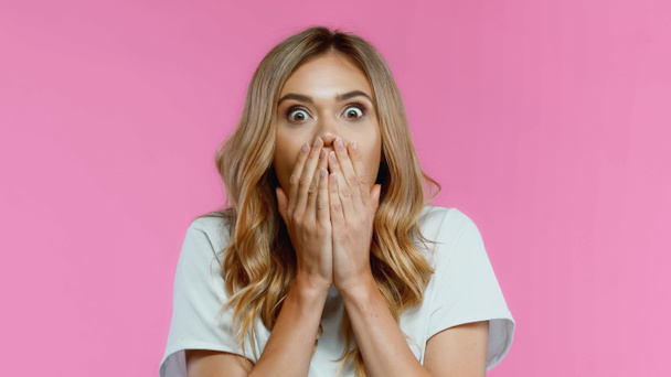 Shocked blonde woman looking at camera while covering face isolated on pink - Fotoğraf, Görsel