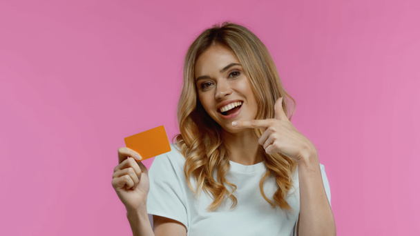 happy woman pointing at credit card isolated on pink - Fotó, kép