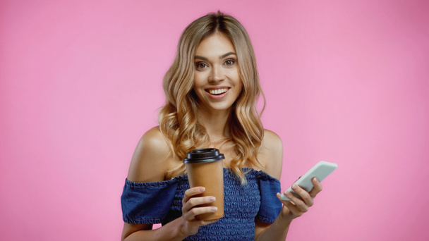 cheerful woman using smartphone and holding coffee to go isolated on pink - Photo, Image