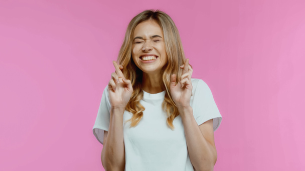 Blonde woman with crossed fingers and closed eyes isolated on pink - Photo, Image