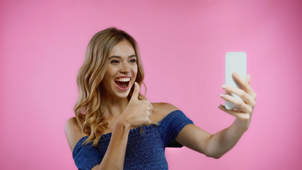 happy young woman showing thumb up while taking selfie isolated on pink  - Foto, afbeelding