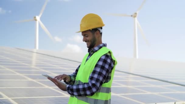 Jonge ingenieur kijkt op digitale tablet naar het nieuwe groene plan voor alternatieve energie met windturbine en zonnepaneel - Innovatie- en groenstroomconcept - Video