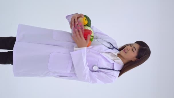 Retrato vertical del joven médico o nutricionista sosteniendo fruta fresca y sonriendo en una clínica. concepto de dieta saludable de los alimentos de nutrición como una receta para la buena salud, la fruta es la medicina - Imágenes, Vídeo