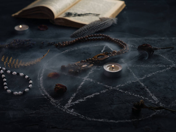 Círculo de pentagrama con una vela, un libro viejo y amuletos sobre la mesa. El concepto de ocultismo, magia oscura, adivinación o Halloween - Foto, Imagen