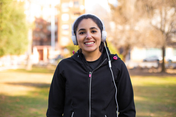 Молода брюнетка спортивна дівчина використовує навушники, що йдуть в парку посміхаючись щаслива і природна
 - Фото, зображення