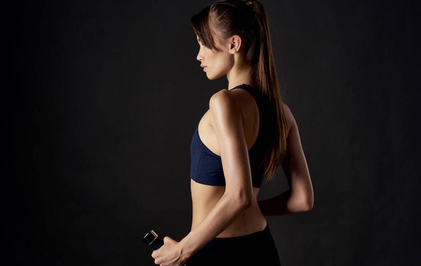 Αθλητική γυναίκα με αλτήρες στα χέρια της σε μαύρο φόντο λεπτή φιγούρα κοντή κορυφή - Φωτογραφία, εικόνα