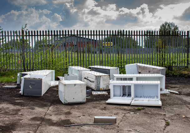 Mehrere ausrangierte Kühlschränke und Gefriertruhen, die auf Betonboden vor einem Sicherheitszaun geworfen wurden, Clayton, Manchester, Großbritannien. - Foto, Bild