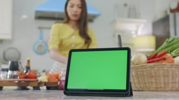 Tableta con una pantalla verde Con un hermoso fondo Cocinar en la casa con una cara feliz, Esposa hace el desayuno feliz en su casa. - Metraje, vídeo