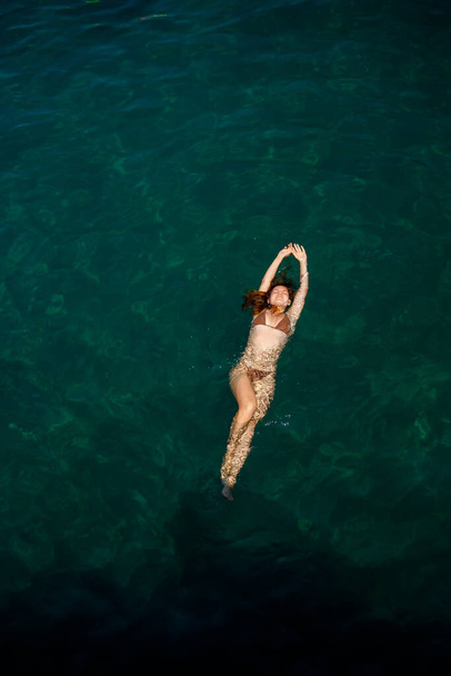 Uma bela jovem mulher atraente em um maiô encontra-se na superfície da água no mar. Vista de cima. Ela está desfrutando suas férias. Foco seletivo - Foto, Imagem