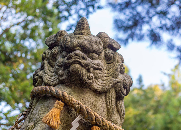 Chien-lion, ou komainu, au sanctuaire shinto de Saiichi, Kanazawa, Japon. Ces statues traditionnelles repoussent les mauvais esprits. Autour de lui se trouve la corde sacrée shimenawa et les banderoles en papier zigzag appelées shide. - Photo, image