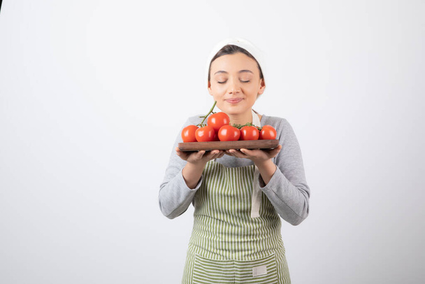 Shot of suloinen nuori nainen haisee punainen tomaatit yli valkoinen seinä - Valokuva, kuva