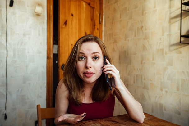удивленная девушка слушает собеседника по телефону, держа голову рукой - Фото, изображение