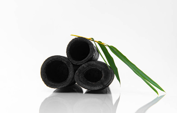 Bamboe geactiveerde houtskoolstokken en groen blad geïsoleerd op witte achtergrond.  - Foto, afbeelding