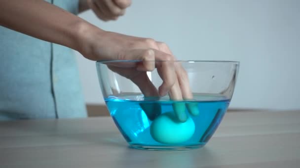 Las manos femeninas teñen los huevos de azul. Ponga los huevos en agua azul teñida. Prepárate para Pascua, tazón de vidrio transparente. Feliz Pascua - Imágenes, Vídeo