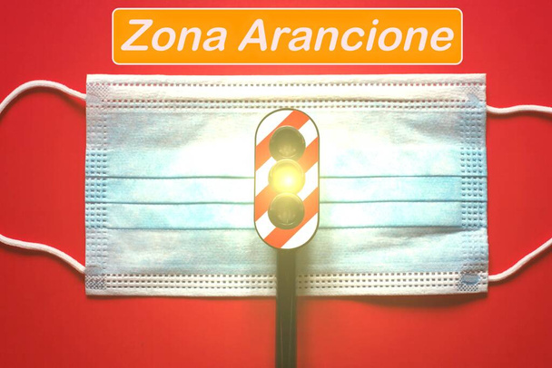 Maska chirurgiczna ze światłem drogowym z żółtym światłem i tekst "zona Arancione" tłumaczący się na pomarańczową strefę, koncepcja pomarańczowej strefy podczas Wirus Corony - Zdjęcie, obraz