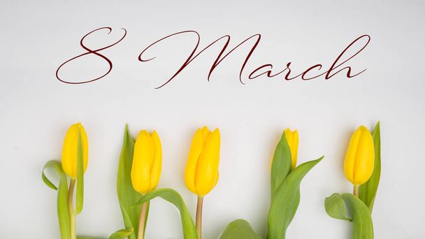 8 marzo texto sobre tulipanes amarillos sobre fondo blanco rústico de madera. concepto de tarjeta de felicitación. sensual tierna imagen femenina. flores de primavera en suave luz del sol de la mañana. plano laico - Foto, Imagen