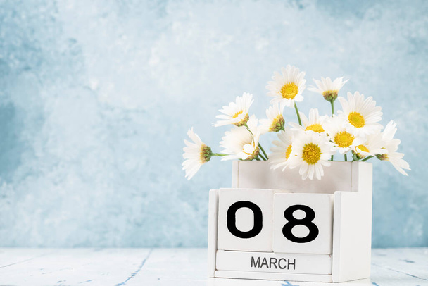 Белый кубический календарь на март украшен цветами маргаритки на синем фоне с копировальным пространством - Фото, изображение