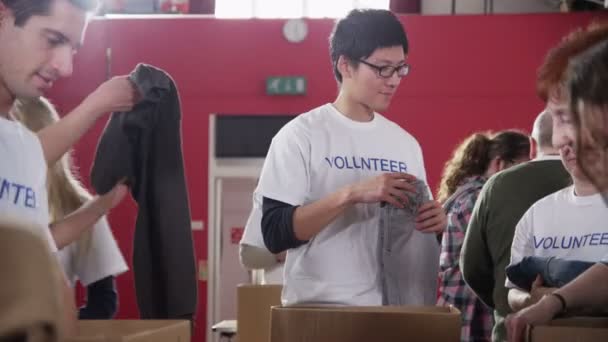 Charity-Freiwillige in bedruckten T-Shirts sortieren Stapel gespendeter Kleidung - Filmmaterial, Video