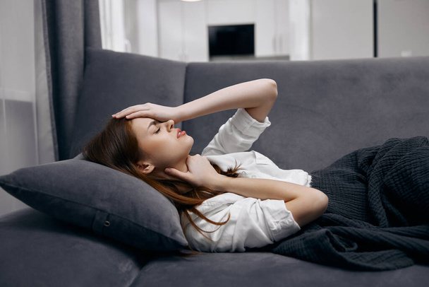 woman at home lies on the sofa covered with a blanket feeling unwell hand on face - Foto, Bild